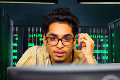 A male looks at a computer screen with server lights in the background.